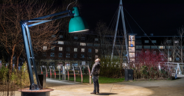 Man standing underneath Lumiere artwork Lampounette which looks like a giant desk lamp.